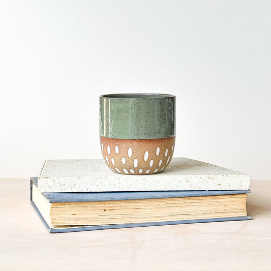 Green ceramic tumbler with a brown base on top of two books against a white background