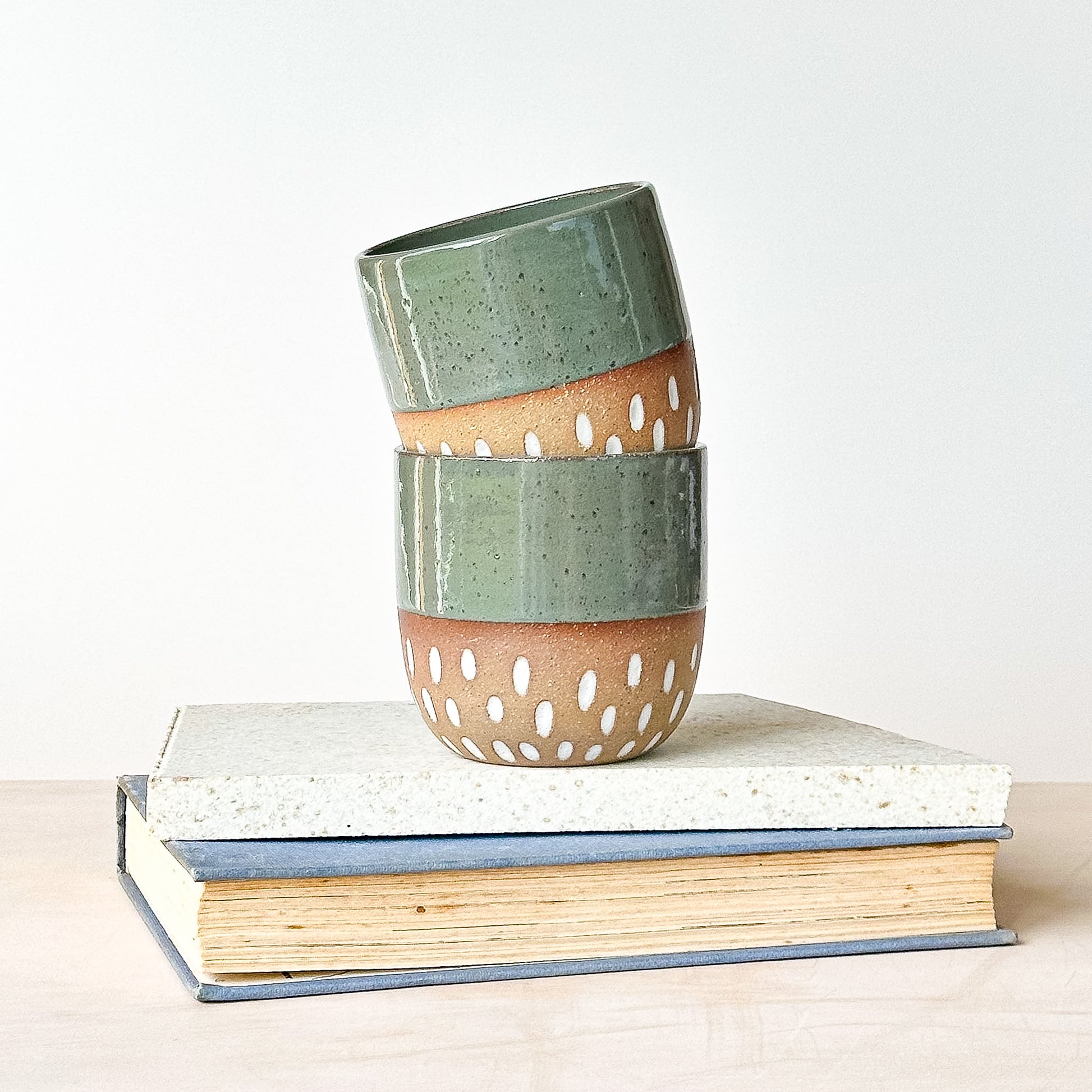 Stack of green ceramic cups with brown accents on a white surface