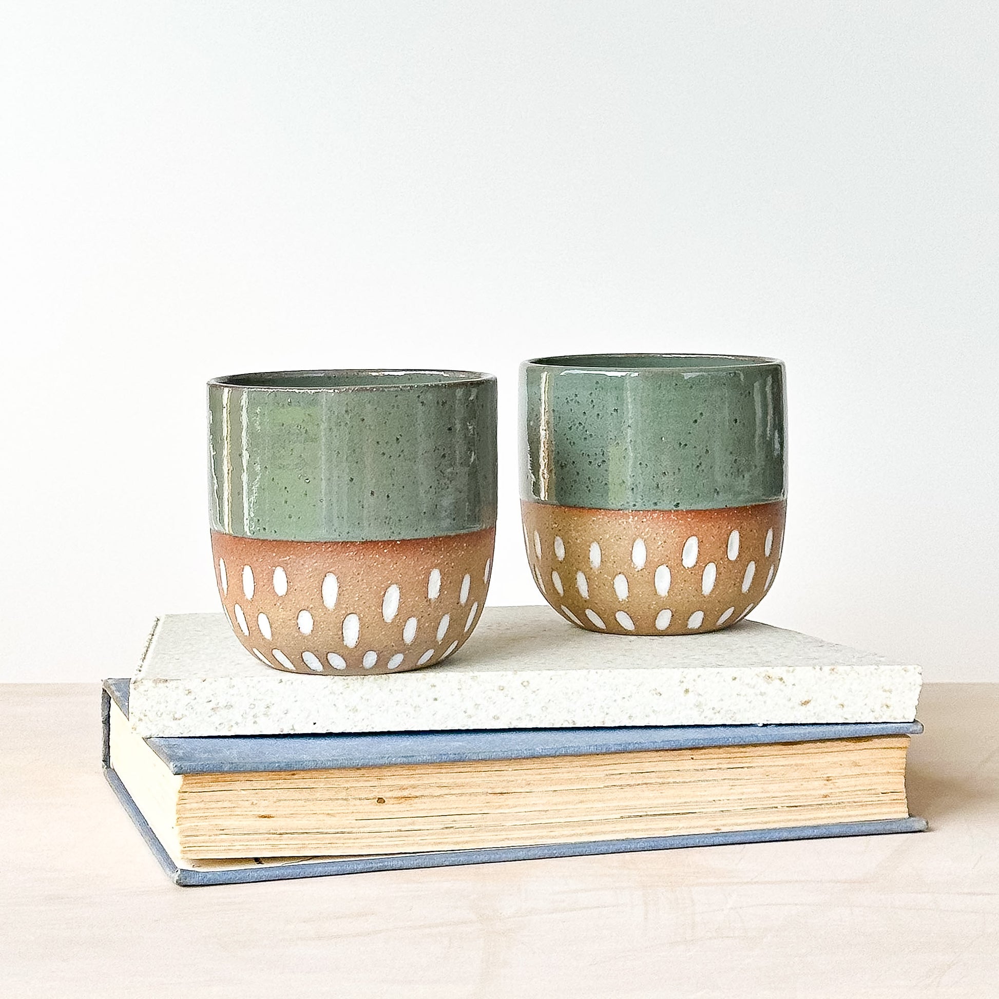 Two ceramic cups with a textured design on top of books against a white background