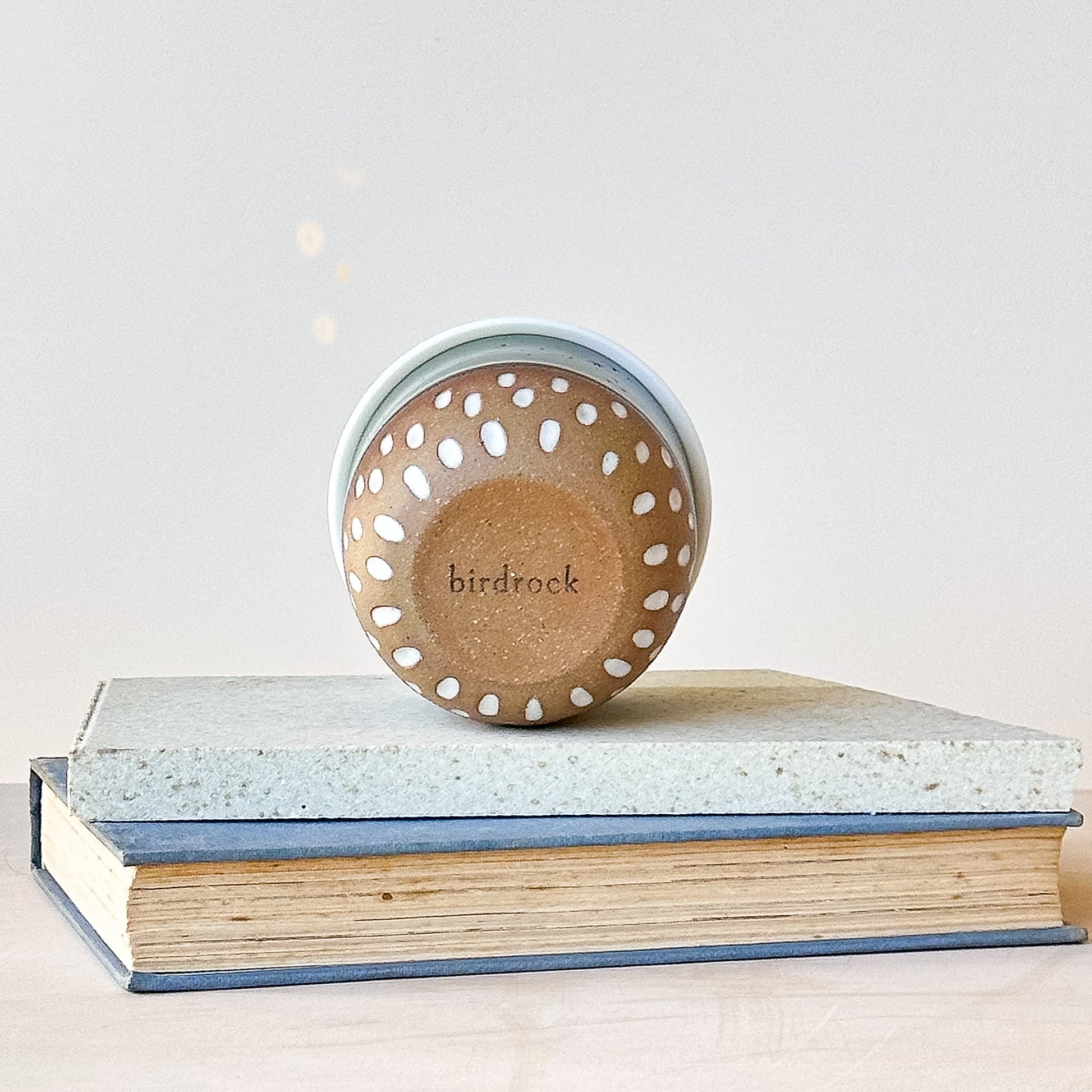 base view of a ceramic keep cup with 'birdrock' branding on a stack of books against a light background