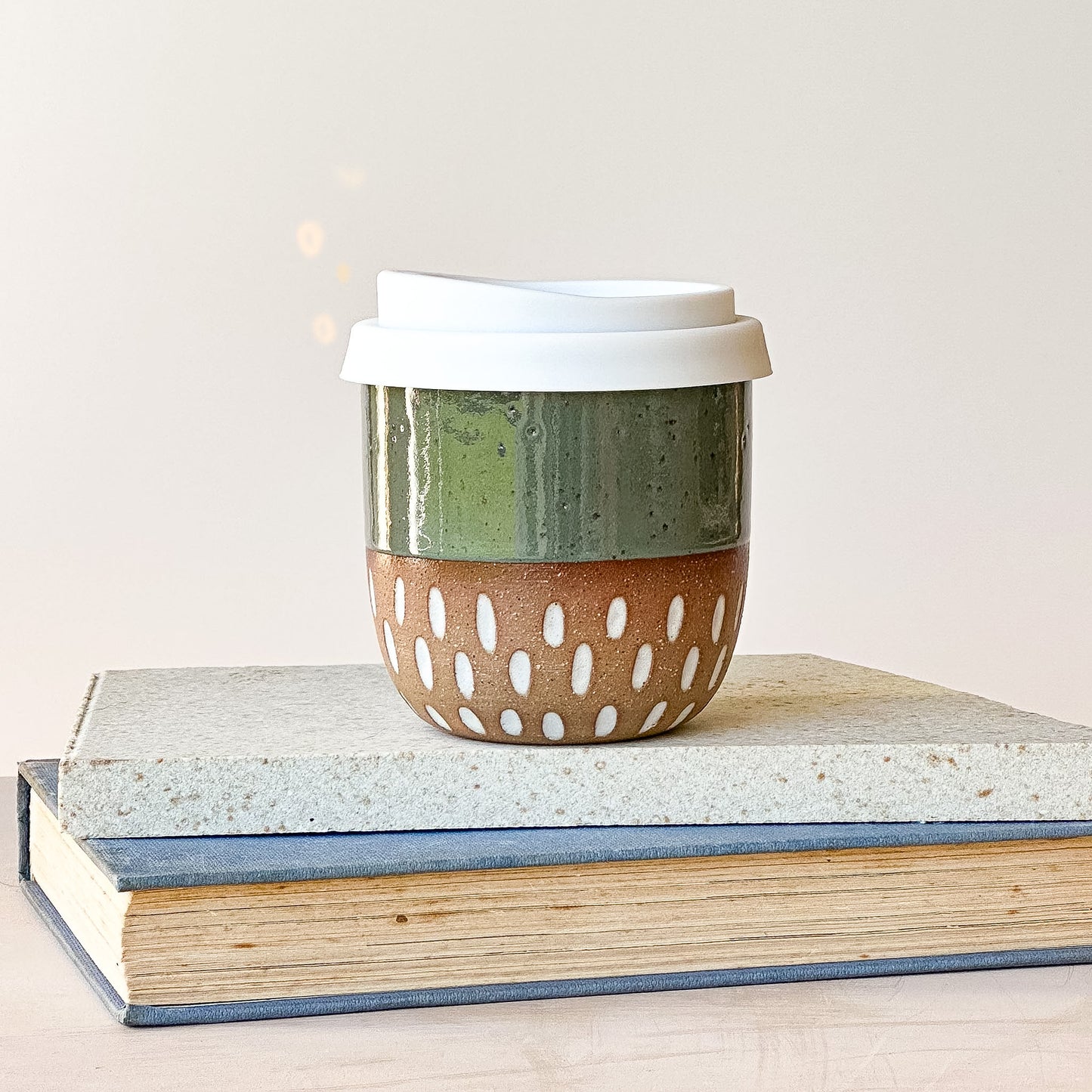 Ceramic travel mug with a white lid on top of books