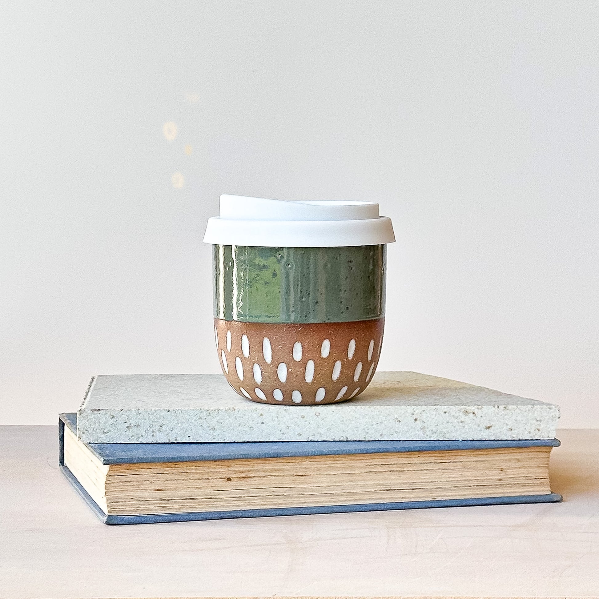 Ceramic coffee cup with a lid on top of books against a light background