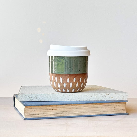 Ceramic coffee cup with a lid on top of books against a light background