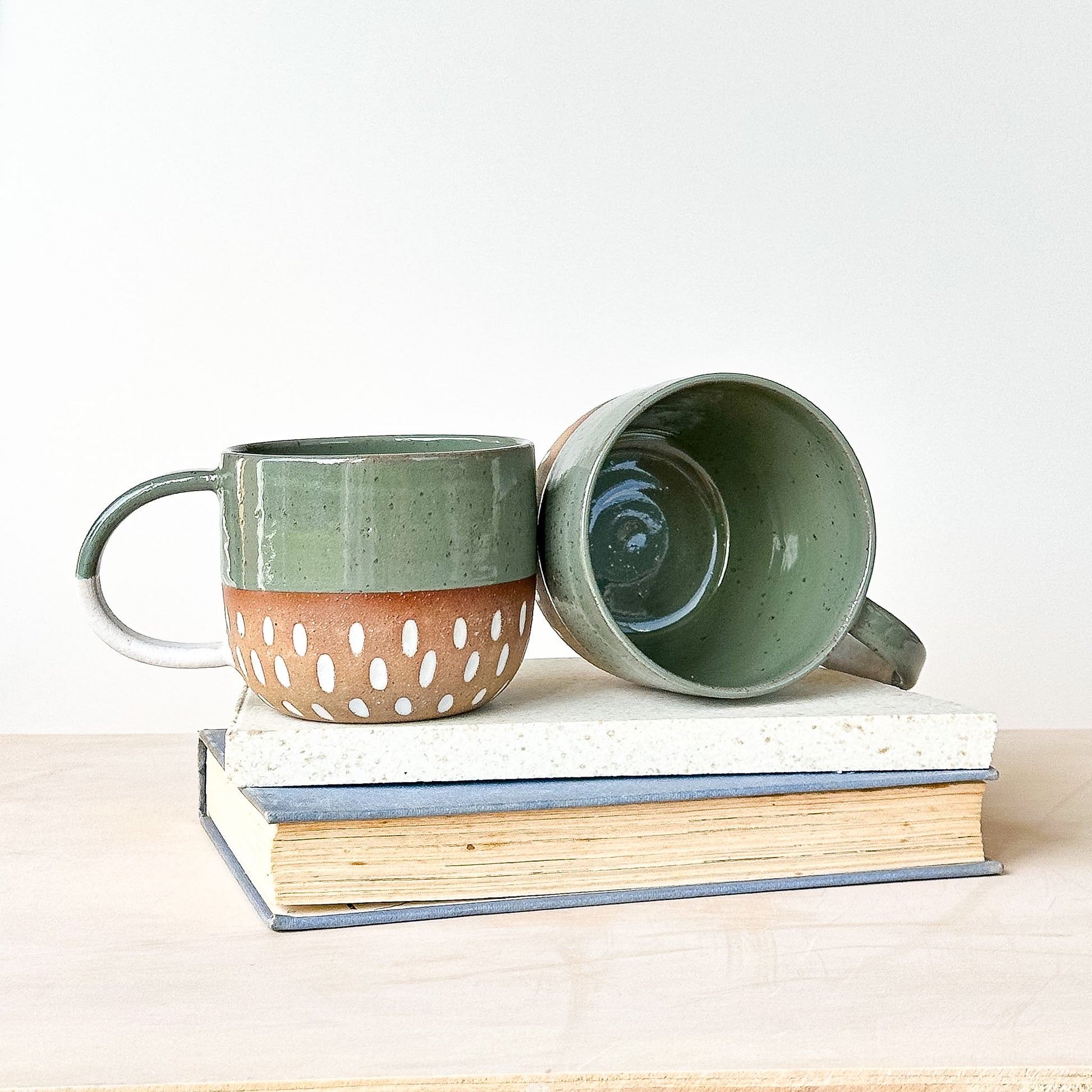 Two ceramic mugs on a stack of books with a plain background
