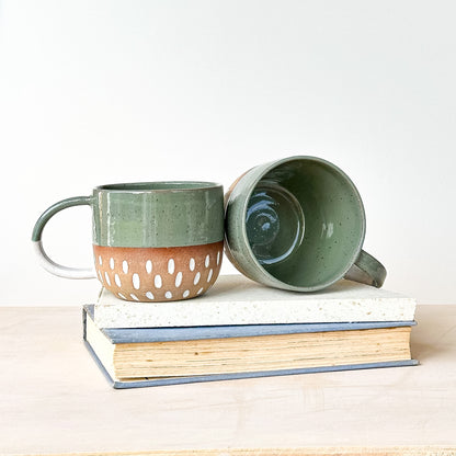 Two ceramic mugs on a stack of books with a plain background