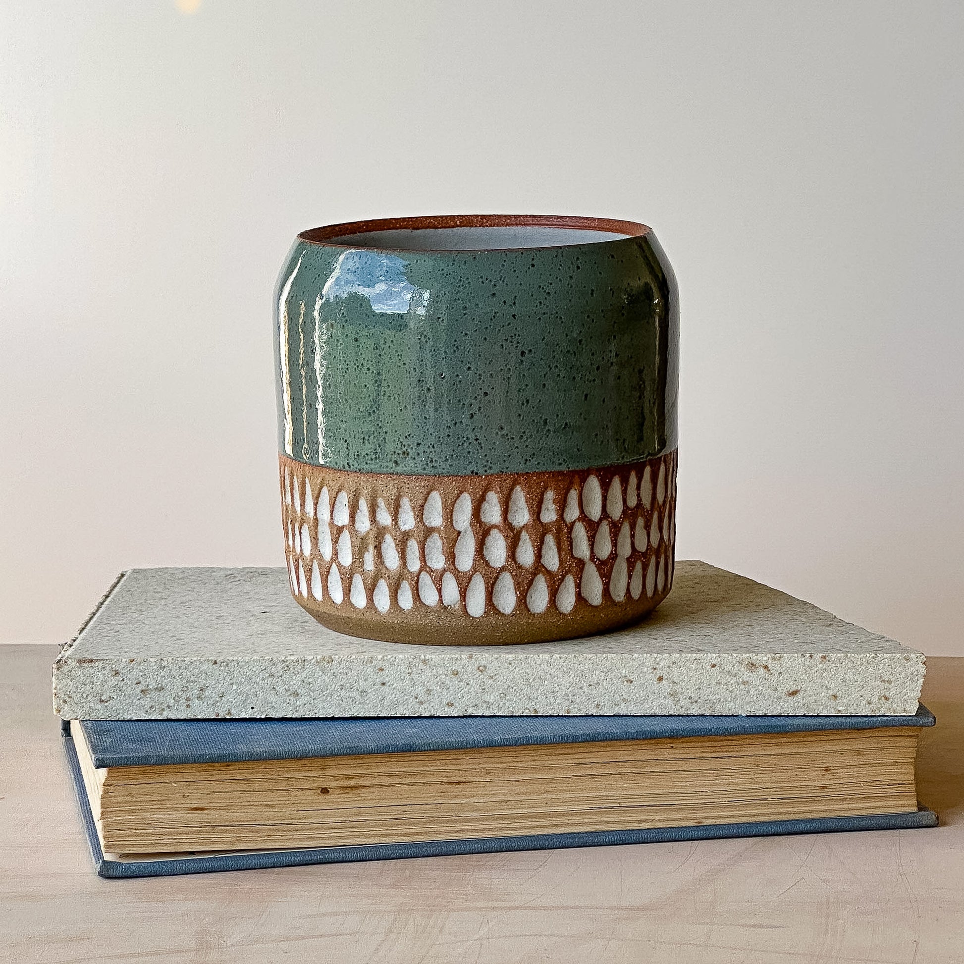 Ceramic pot with green and brown design on top of two books