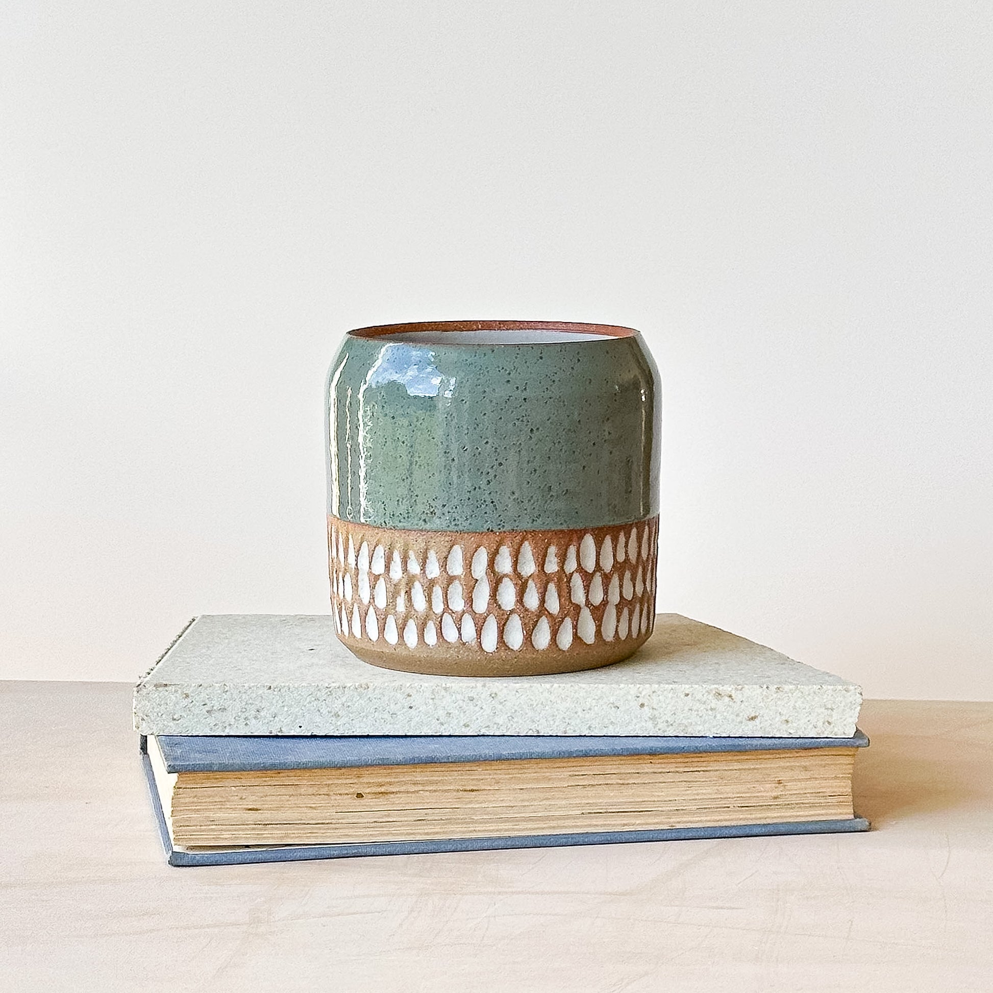 Ceramic pot with decorative pattern on top of two books against a light background