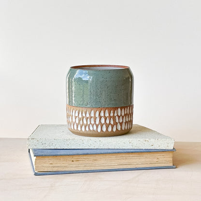 Ceramic pot with decorative pattern on top of two books against a light background
