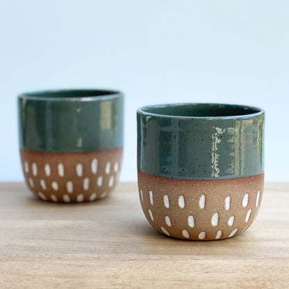 Two ceramic cups with green top and brown bottom featuring white dot patterns on a wooden surface.
