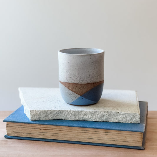 A ceramic cup sitting on a tile and a book with a neutral background