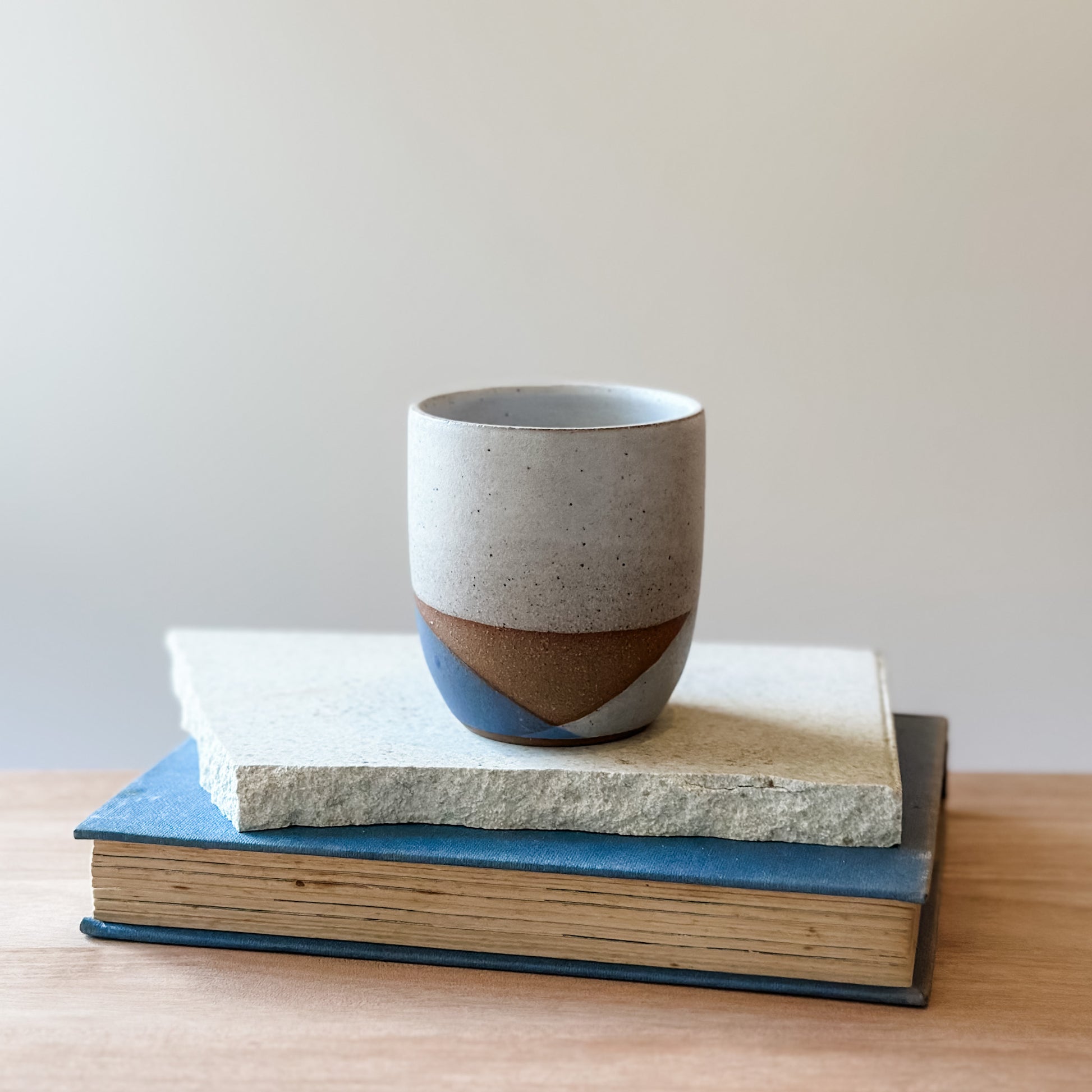 Ceramic cup with two-tone design on top of two books on a wooden surface.