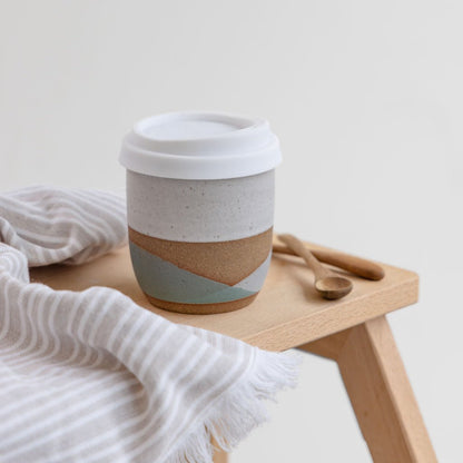 A view of the large tidal handmade ceramic keep cup in green and glaze glaze. The handmade ceramic keep cup is sitting on top of a wooden stool in coastal styled setting.