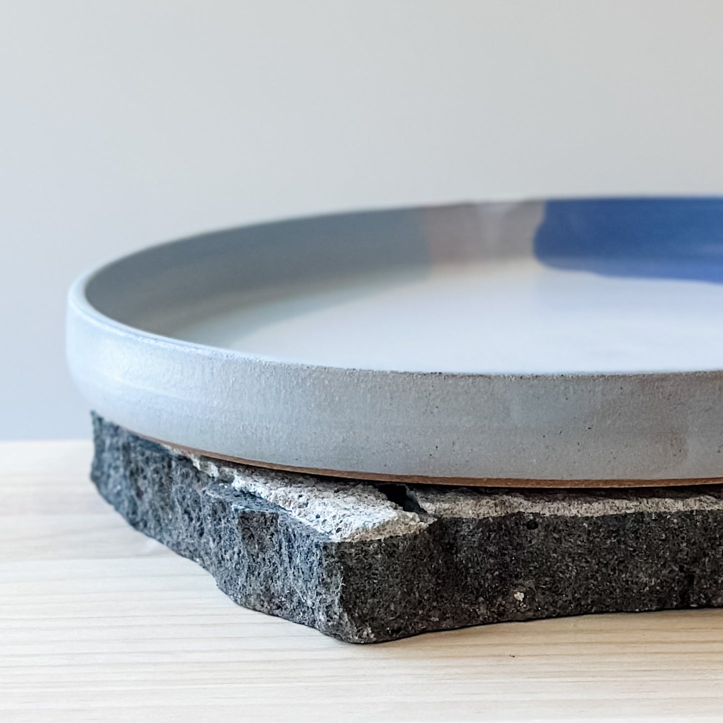 A close-up view of the medium Tidal Handmade Ceramic Platter in violet, blue-grey and white glaze. The platter sits on a tile and a wooden table.
